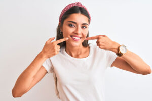Young beautiful woman wearing casual t-shirt and diadem over isolated white background smiling cheerful showing and pointing with fingers teeth and mouth.