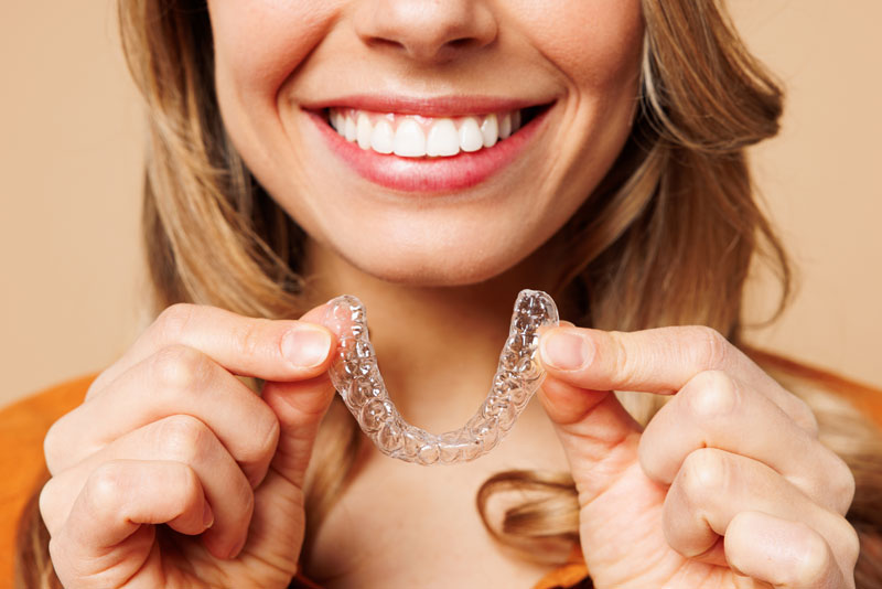Close up cropped young woman wear orange shirt casual clothes hold in hand invisible transparent aligners,