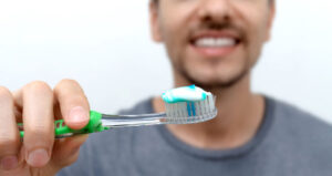 Young smiling man brushing his teeth. Oral hygiene with toothbrush and toothpaste. World Oral Health Day. Cleaning and brushing teeth with fluoride.