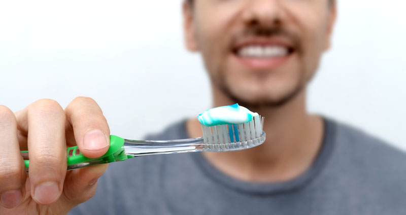 Young smiling man brushing his teeth. Oral hygiene with toothbrush and toothpaste. World Oral Health Day. Cleaning and brushing teeth with fluoride.