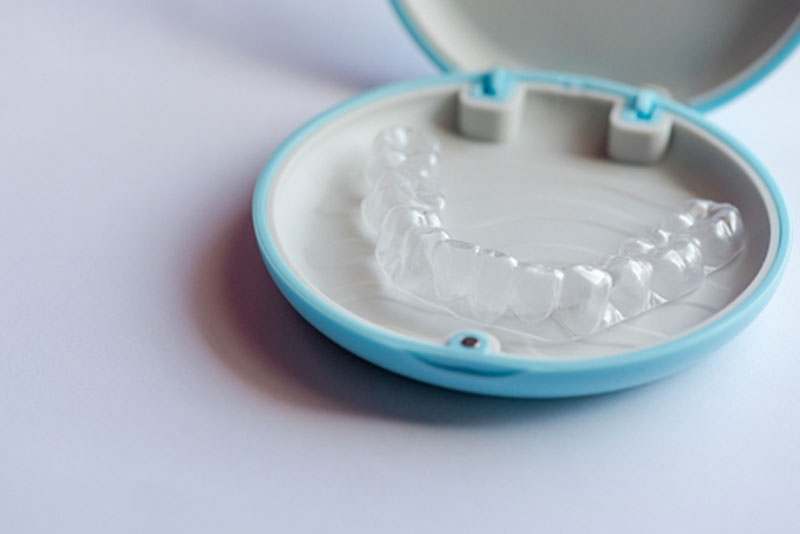 Clear Invisalign aligner in an open blue storage case on a white background.