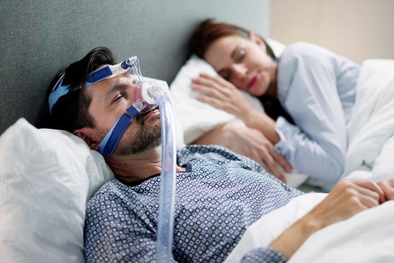 Man sleeping with a CPAP machine to manage sleep apnea, promoting better breathing and restful sleep—effective treatment for obstructive sleep apnea.