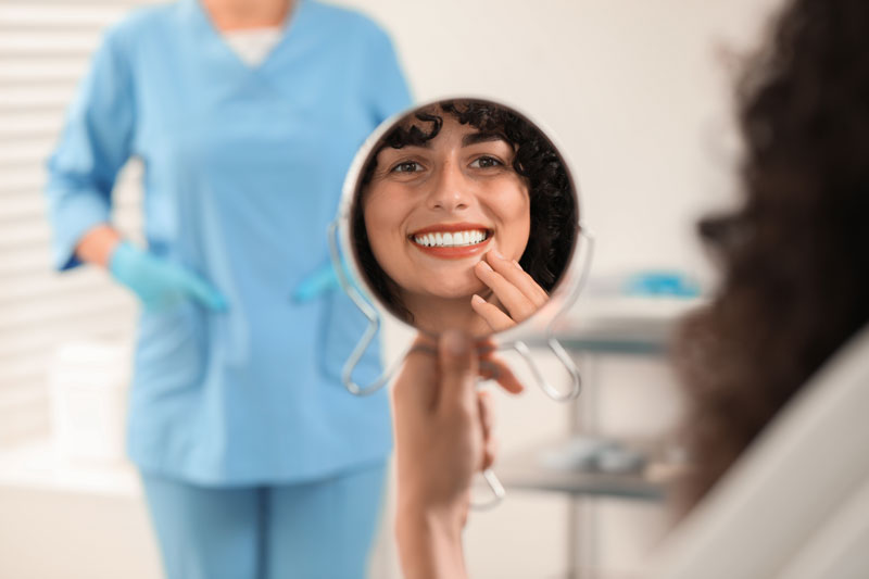 3D illustration of a dental implant with a metal post, abutment, and crown being placed in the lower jaw, surrounded by natural teeth and gums