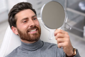 Man looking at his new dental implants in mirror indoors
